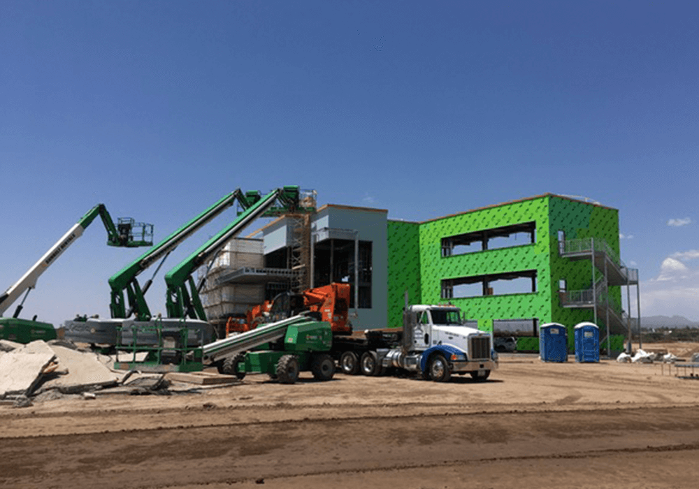 Cranes are lifting roofing materials onto a new construction project in preparation for a commercial roofing installation