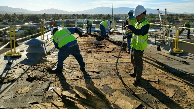 Roofing contractors are using shovels to remove old roofing materials from a commercial roof to prepare it for a new roof installation